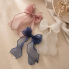 Three large organza bow clips in dusty rose, deep blue, and creamy white, featuring flowing sheer ribbons, arranged on a light surface.