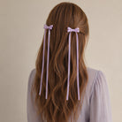 Lavender ribbon bow clip set with long tails, styled in wavy brown hair, seen from the back.