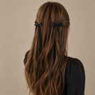 Black ribbon bow clip set featuring two bows on each side with long trailing ribbons, worn in wavy brown hair.