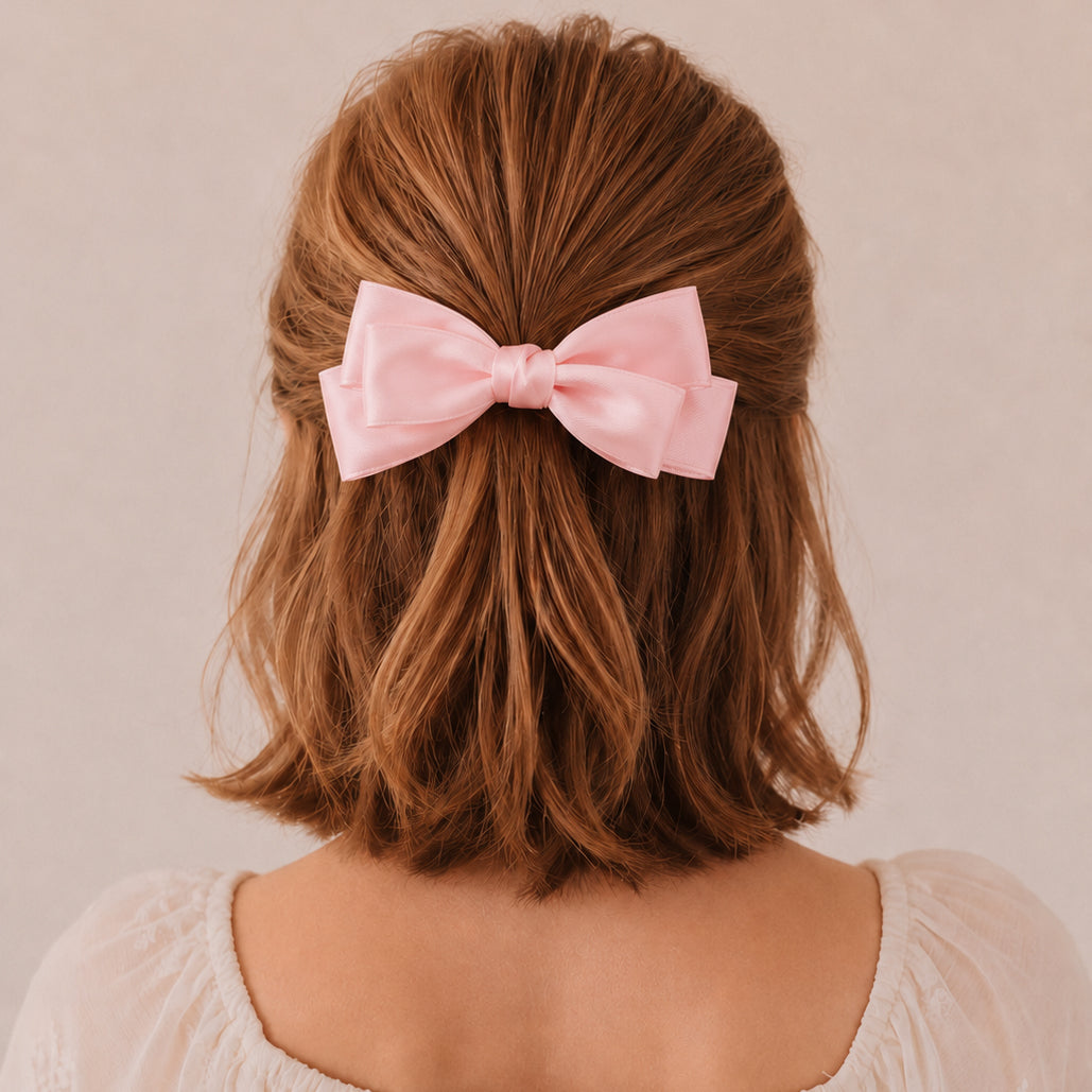 Large blush satin double bow clip worn in wavy brown hair, seen from the back.