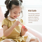 A smiling child in a yellow dress sits on a pink surface, painting her nails with a red bottle of nail polish. Text in a white box to the right reads "Kid-Safe."
