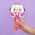 Hand holding a pink cartoon-style princess sheep hand mirror against a purple background.