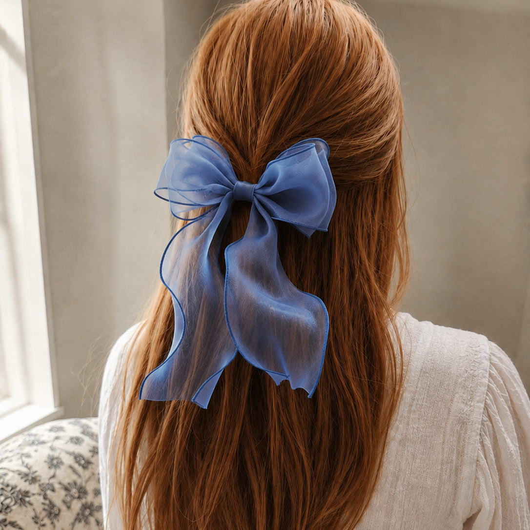 Large blue organza bow clip in reddish-brown hair, with long flowing ribbons and a subtle sheen.