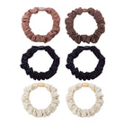 Set of six neutral-colored scrunchies: light pink, brown, black, and cream soft gathered fabric with plastic connectors.