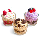 Three Jellycup sox wax candles designed to look like dessert parfaits in clear glass cups, each topped with piped whipped-style wax and decorative accents—strawberries and sprinkles on a vanilla design, chocolate cookies and pieces on a caramel design, and mixed berries on a lavender design.